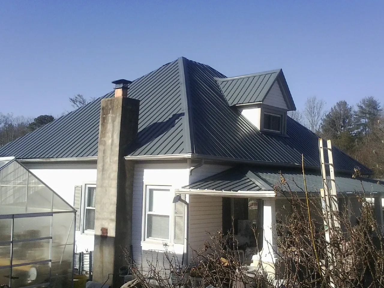 Dark blue standing seam metal roof on a white farmhouse with dormer — Slate & Tile Roof Repair by Roofing Brothers in Oriska
