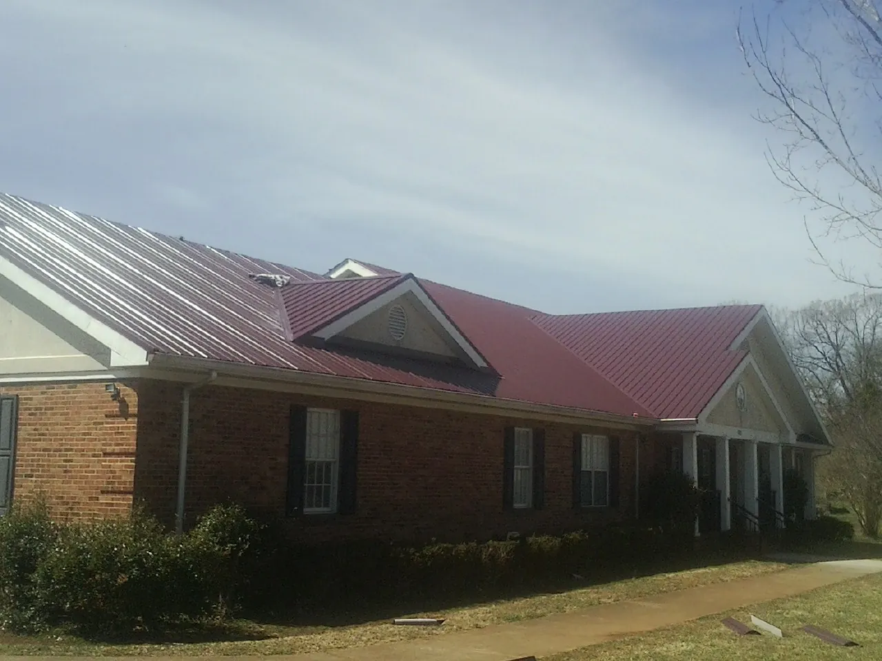 Red metal roof with gabled entries on a long brick building, from a Hail Damage Roof Repair job in Oriska