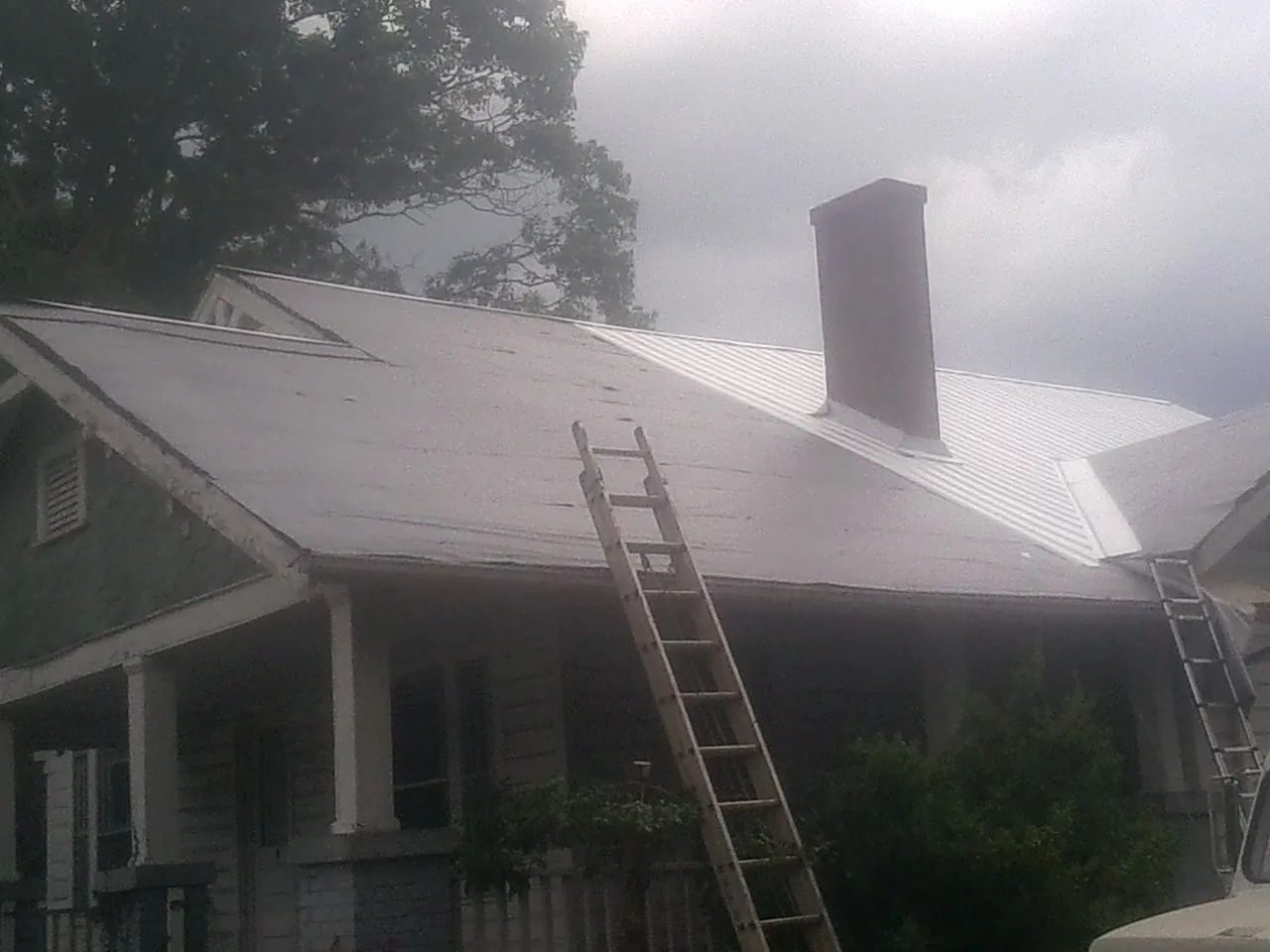 Ladders against a metal roof on an older home with a brick chimney in Oriska