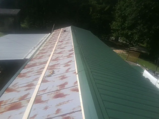 Old rusted panels beside newly installed green metal roofing — Wind Damage Roof Repair by Roofing Brothers in Oriska