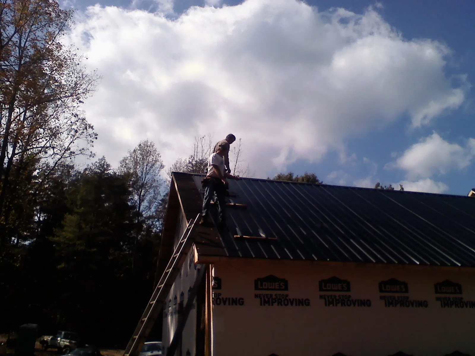 Roofer fastening dark metal panels high against a cloudy sky, from a Roof Inspection job in Oriska