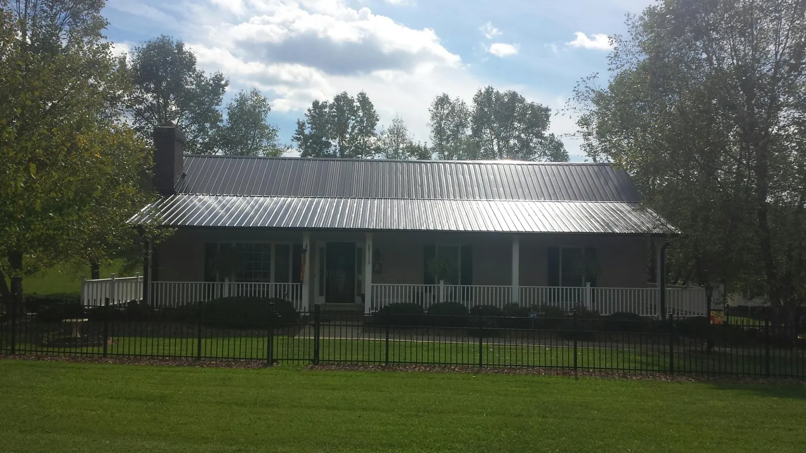 Gray metal roof on a brick ranch with a full width front porch — Gutter Guard Installation work by our crew in Oriska