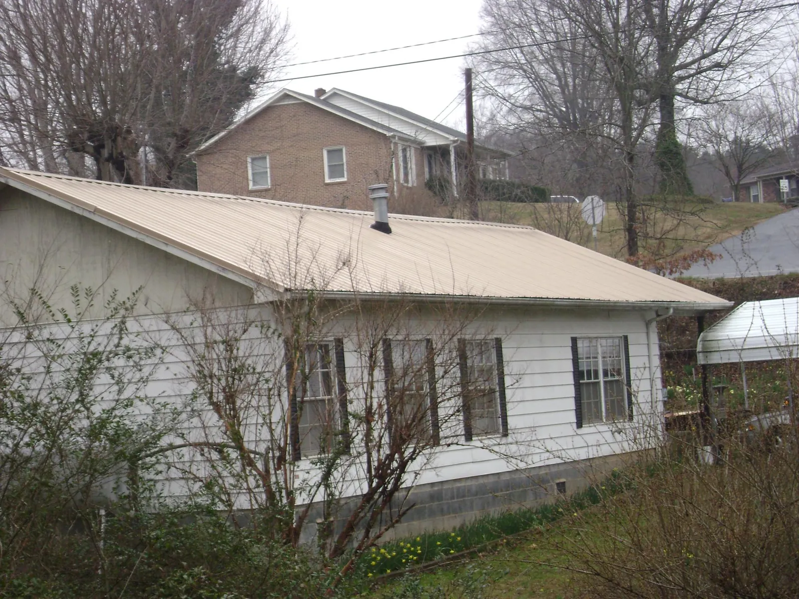 Tan metal roof on a white sided house set into a hillside — Commercial Roofing by Roofing Brothers in Oriska