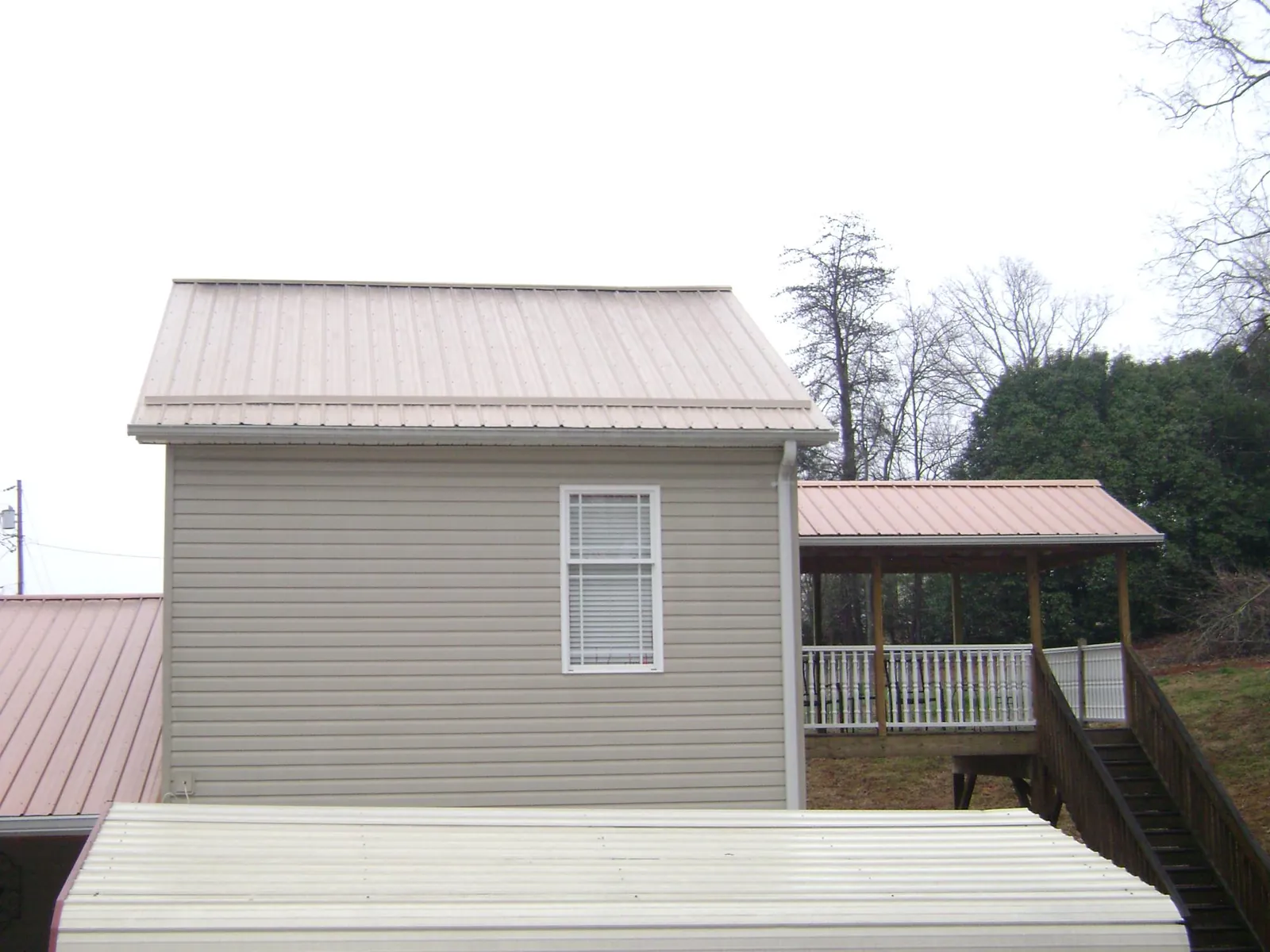 Tan metal roofs on a two story addition and attached porch, from a Roof Replacement job in Oriska